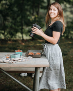 Jenn Bakos at a table outside enjoying fresh air and photagraphing fruit while wearing a grey dress and black top